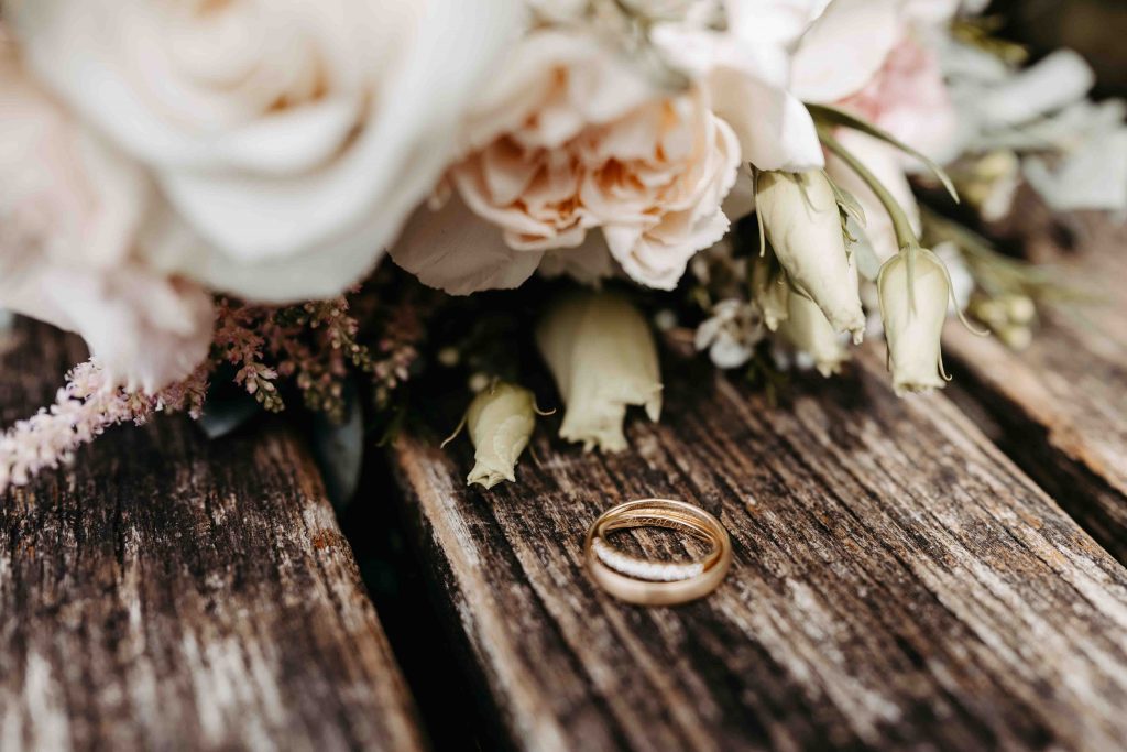 Die Eheringe liegen ineinander. Man kann das eingravierte Hochzeitsdatum lesen. es liegt ein Brautstrauß daneben