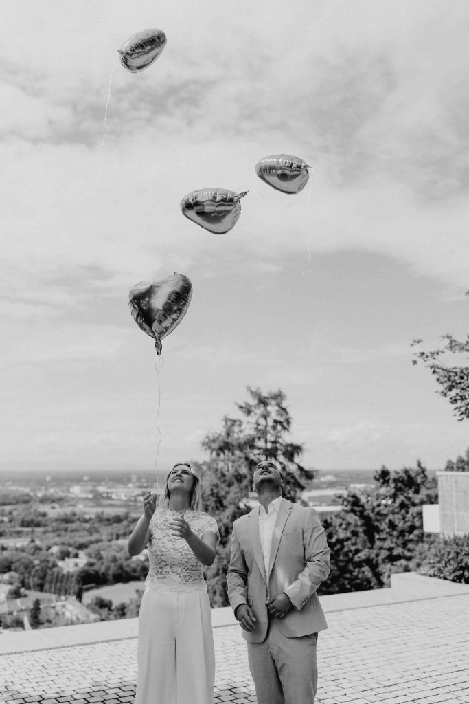 Das Brautpaar lässt Luftballons steigen. Man sieht im Hintergrund die Stadt Karlsruhe. Das Paar befindet sich auf dem Turmberg vor dem Standesamt.