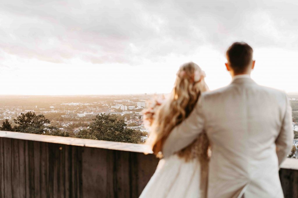 Blick über Karlsruhe vom Turmberg aus. Brautpaar ist im Vordergrund verschwommen. Das Paar schaut mit dem Rücken zur Kamera gedreht auf die Stadt
