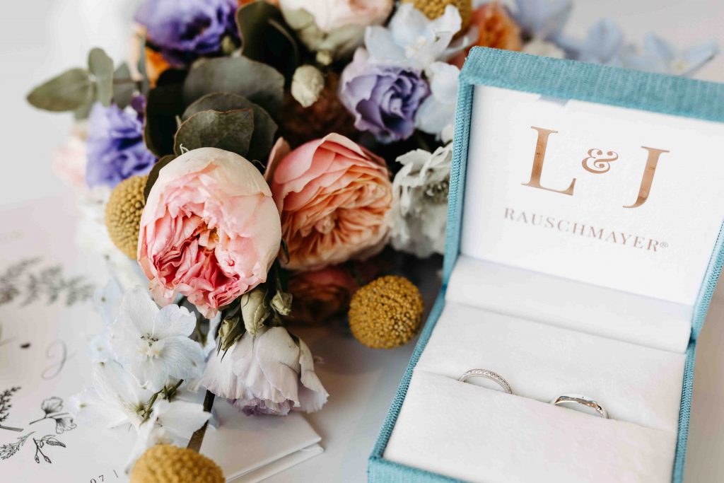 Flatlay-Foto. Brautstrauß mit Ringschachtel und den Eheringen ist zu sehen. Liebevoll arrangiert