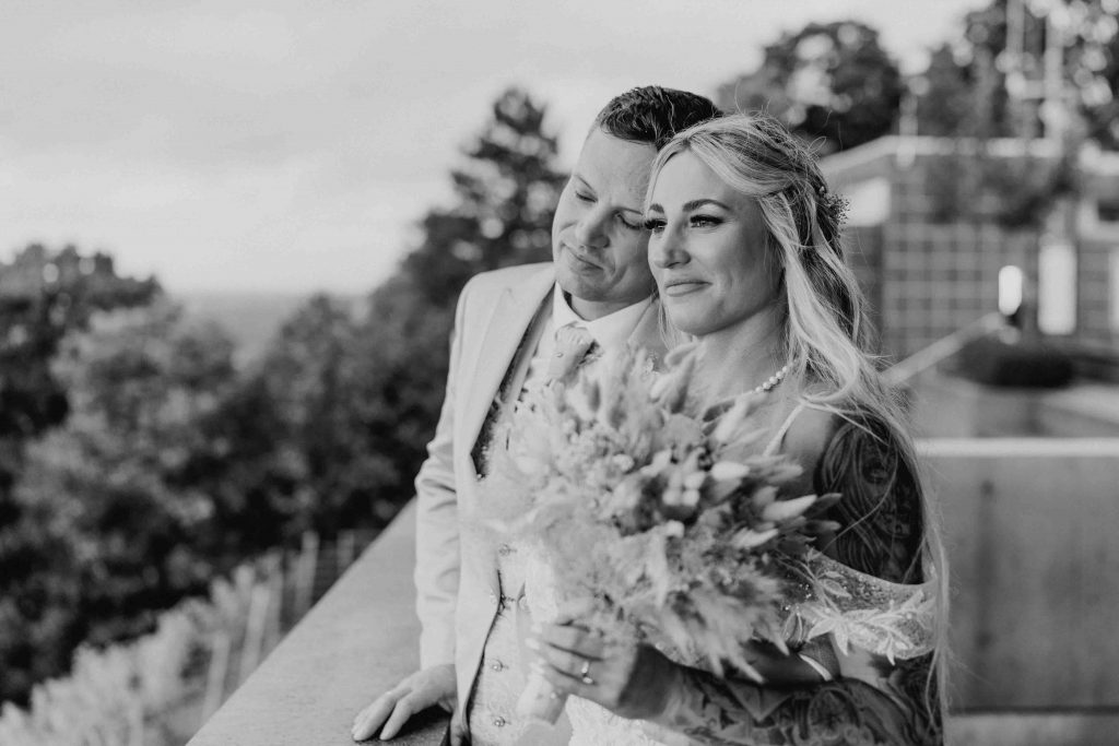 Brautpaar steht auf dem Turmberg vor dem Standesamt Durlach. Braut schaut in die Ferne und Bräutigam steht neben ihr und lehnt liebevoll seinen Kopf gegen ihren. Er hat die Augen geschlossen