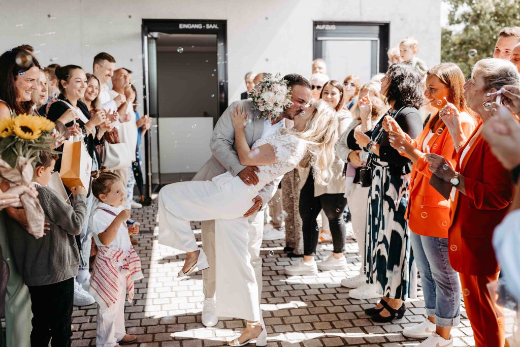 Das Brautpaar läuft durch das Spalier und küsst sich dabei. Ein Dip-Kiss. Die Leute im Spalier pusten Seifenblasen.
