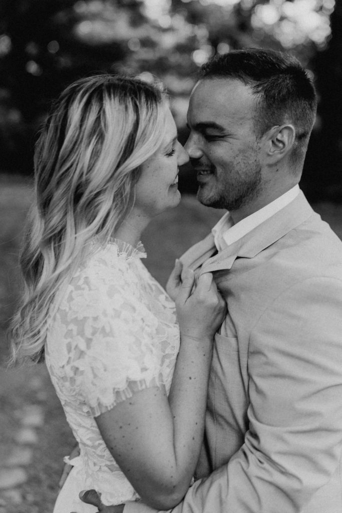 liebevoller, zärtlicher Nasenküss eines Brautpaares. Beide lächeln sich dabei an. Der Blick der beiden geht auf den jeweiligen Mund. Sie zieht ihn mit ihren Händen an seinem Riviere zu ich, als wolle sie ihn küssen. Er umarmt ihre Hüfte