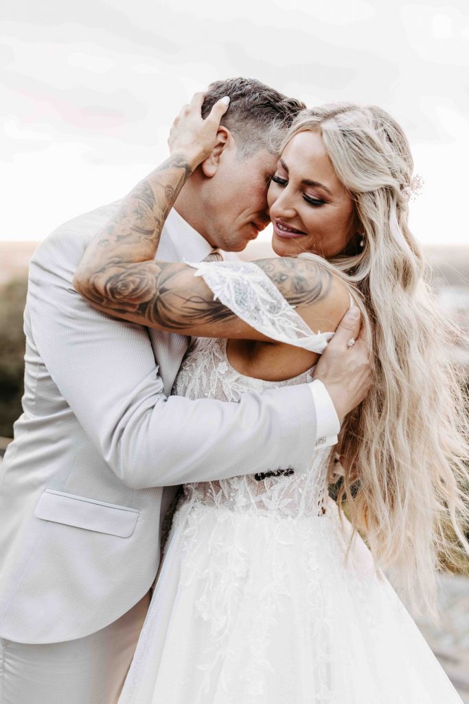 Hochzeitsfotograf Karlsruhe: eng umschlungenes Brautpaar. Er ist gerade dabei, sie am Hals zu küssen. Ihr Blick geht Richtung Boden, sie lächelt glücklich