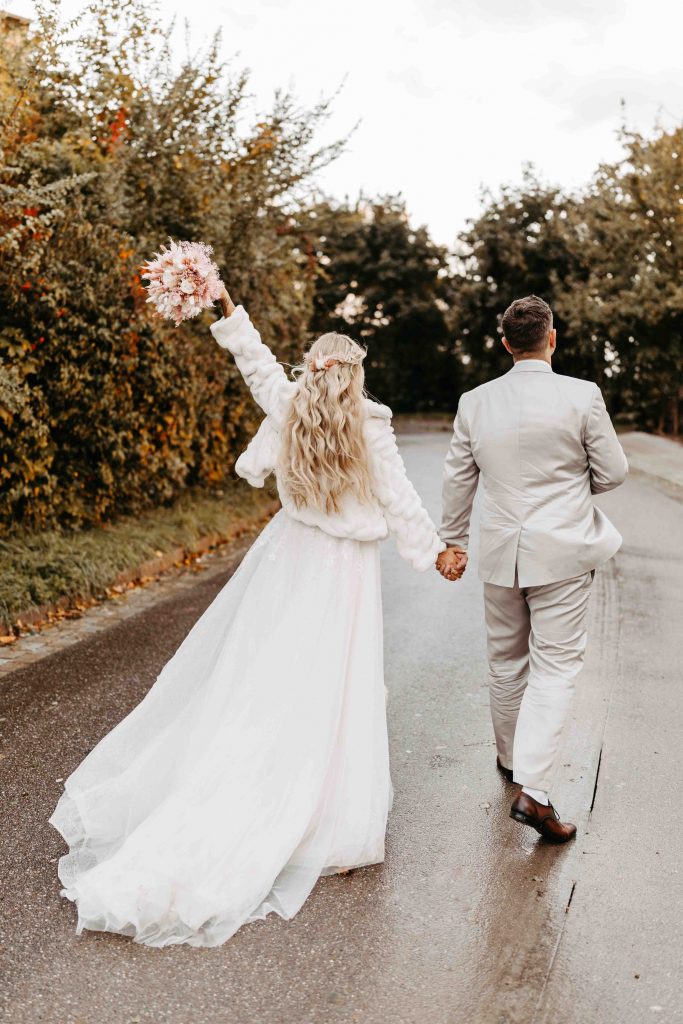 Hochzeitsfotograf Karlsruhe: Brautpaar von hinten. Sie halten Händchen und sie jubelt ihren Brautstrauß in die Luft