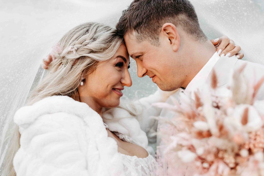 Hochzeitsfotograf Karlsruhe: Ein Bild unter dem glitzernden Schleier. Das Brautpaar hat die Stirne aneinander gelegt und blickt sich tief in die Augen und lächelt. Sie umarmt ihm im Genick.