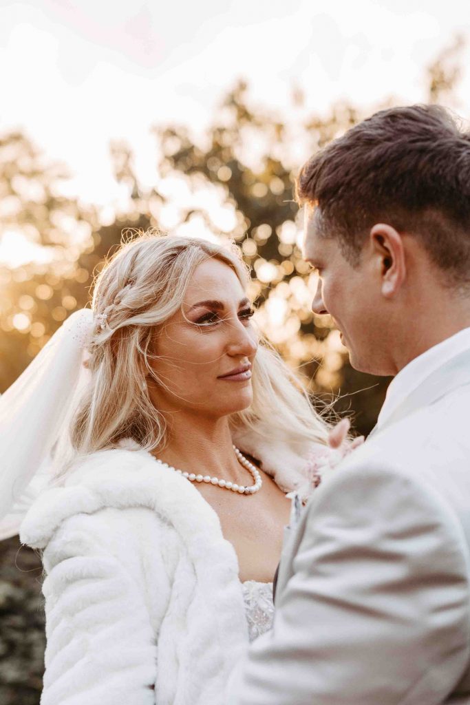 Hochzeitsfotograf Karlsruhe: Das Brautpaar schaut sich tief in die Augen. Die Sonne geht im Hintergrund unter und funkelt durch die Bäume im Hintergrund. Der Wind weht durch die Haare der Braut