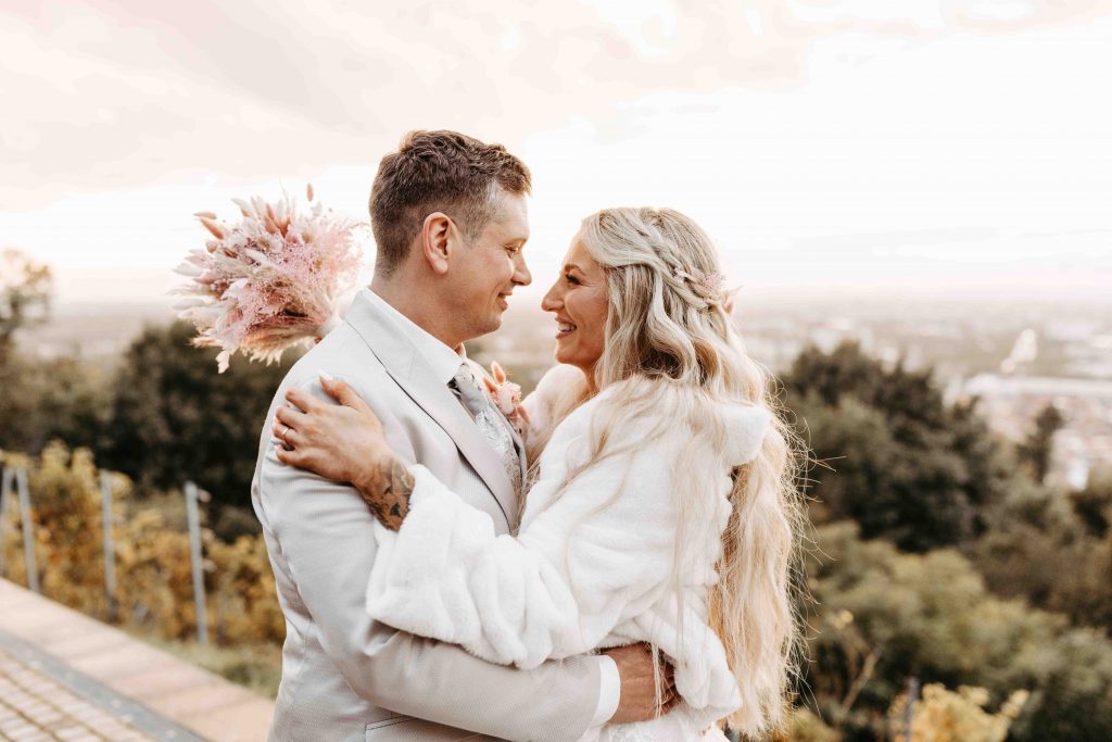 Das Brautpaar steht beim Sonnenuntergang vor den Weinreben auf dem Turmberg in Karlsruhe Durlach. Im Hintergrund sieht man verschwommen die tolle Aussicht über die Stadt Karlsruhe